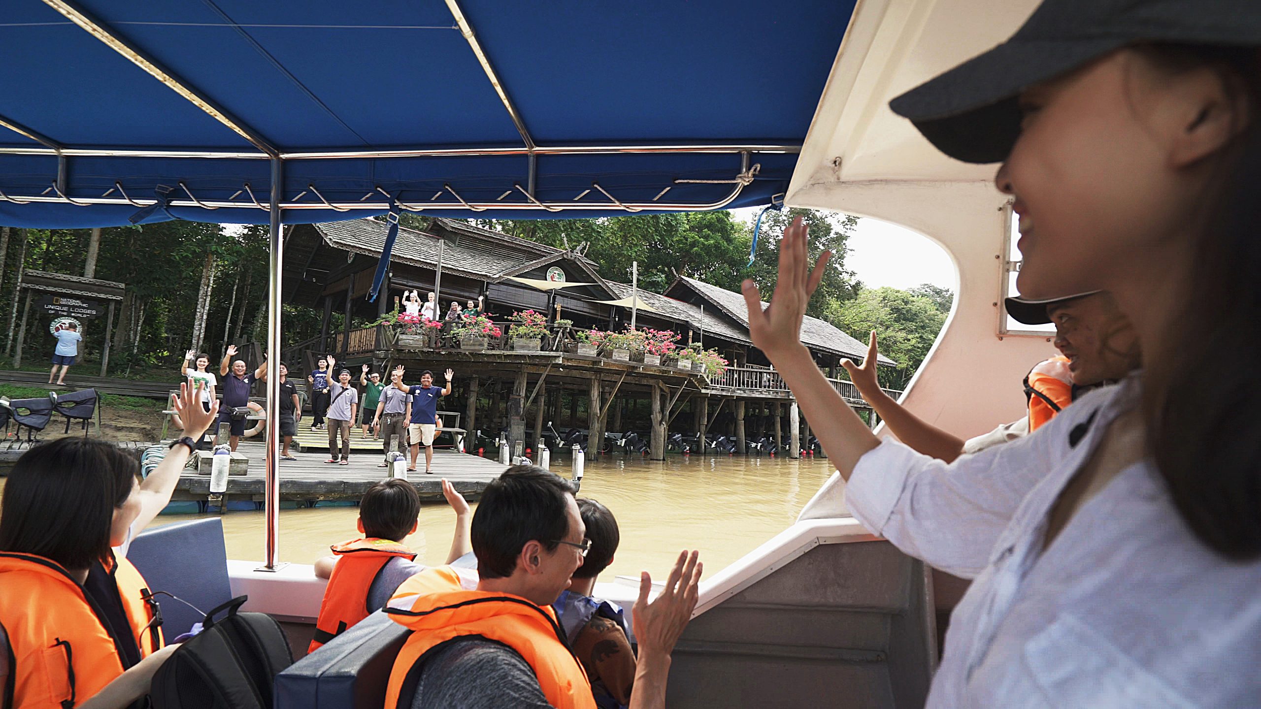 Departing guests waving goodbye from the boat to the staffs of Sukau Rainforest Lodge